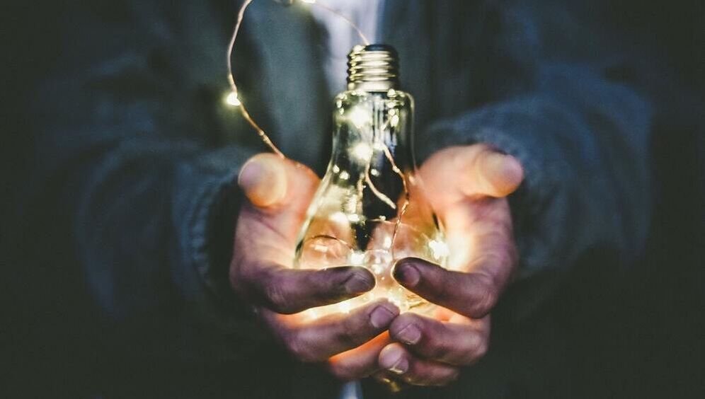 Image of a man's hands holding out a lightbulb with glowing fairy lights inside it.